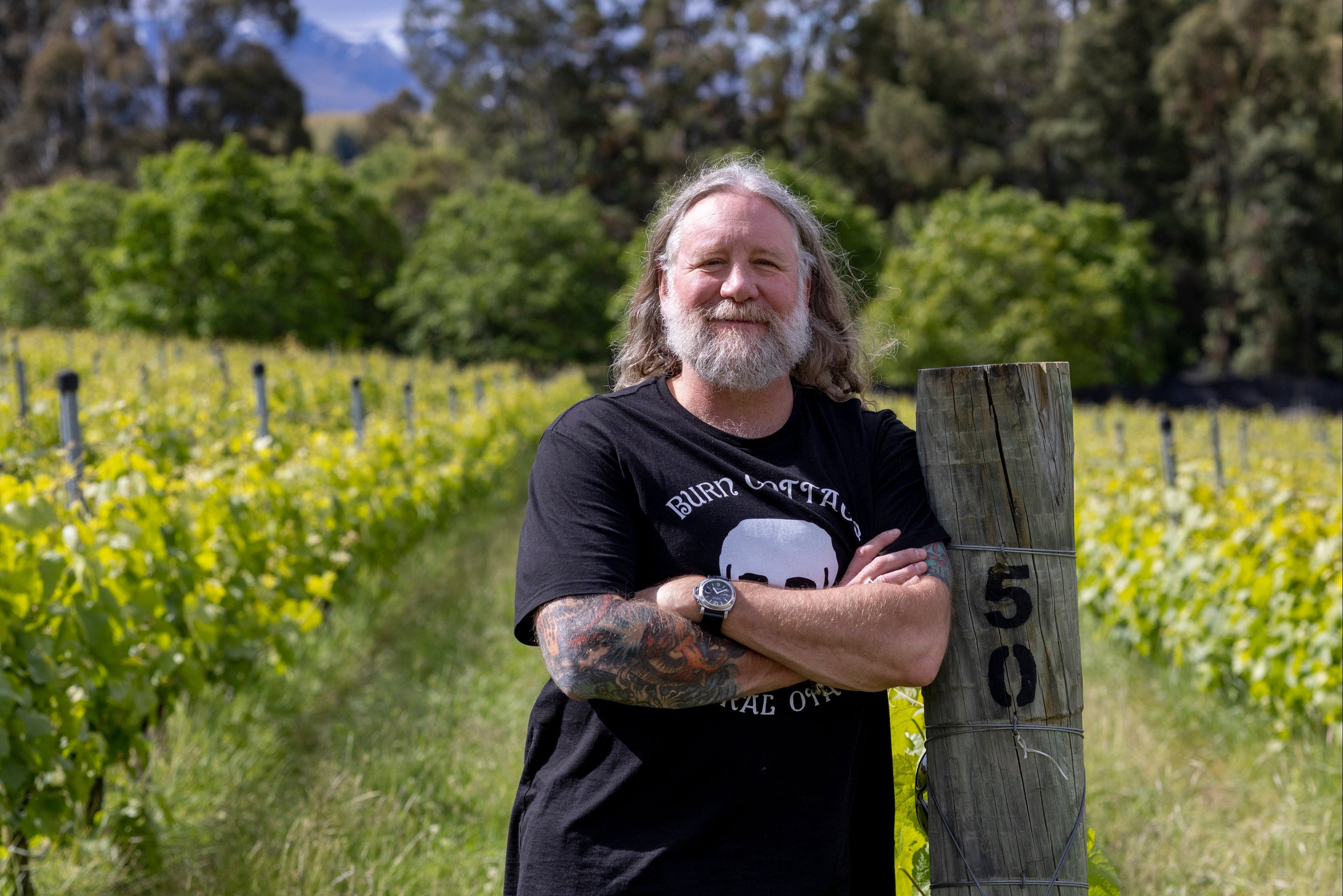 Man standing in a vineyard with trees and mountains in the background